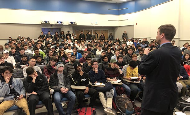 A student speaks to a large group of students in an auditorium