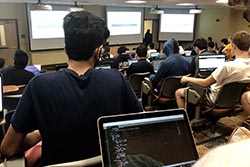 Students in an auditorium work on their laptops.